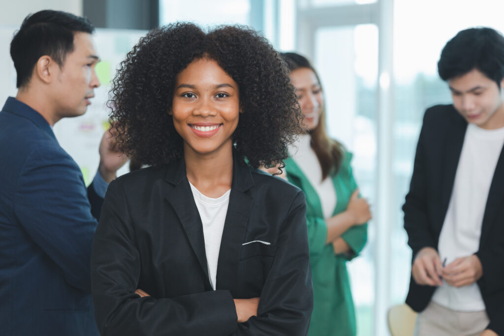 A smiling young professional standing in a modern office setting with her team standing behind her.