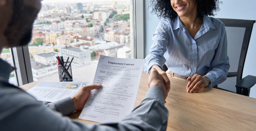 A young professional shaking hands with a hiring manager after signing an employment contract.